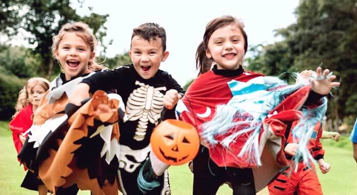 Fröhliche Kinder, die an Halloween mit Karnevalskostümen in der Natur herumlaufen